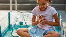 Petite fille assise dans le parc à hamster Omlet avec son hamster et ses accessoires