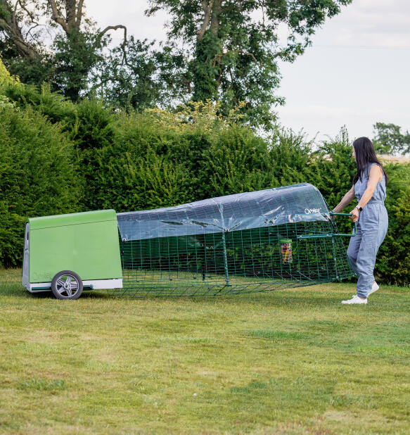 Femme déplaçant le poulailler portable Eglu Go dans une arrière-cour