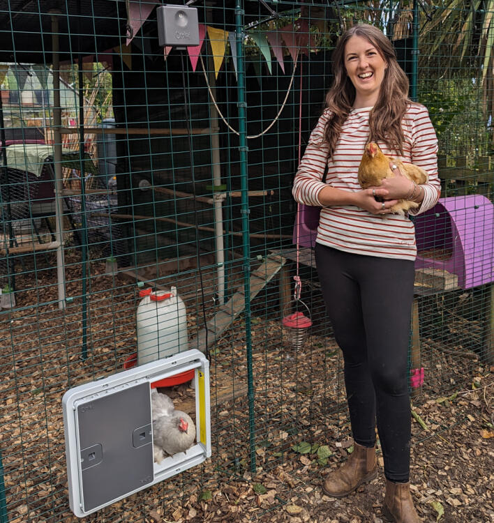 Femme tenant un poulet devant son poulailler avec porte automatique